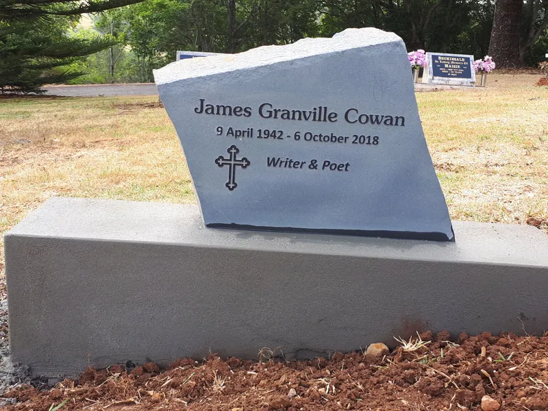 Rock-pitched natural stone headstone with engraved cross on a grey base