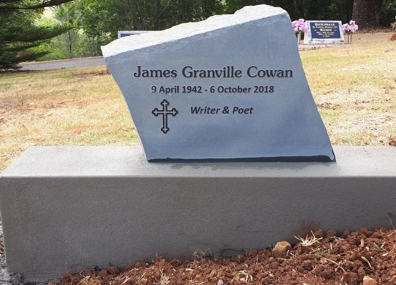 Local basalt headstone with a raised inscription and cross on a rendered foundation