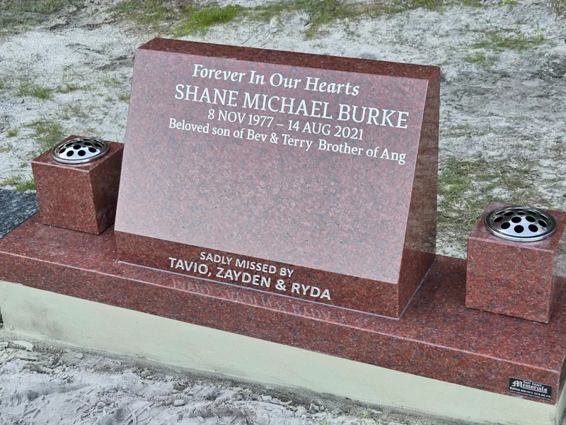 Close view of a red granite headstone and vase on a polished base